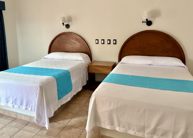 Two beds with white bedspreads an aqua blue bed runner and warm wood headboard.