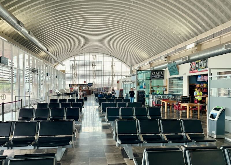 The inside of an airport with a convex roof and black chairs.