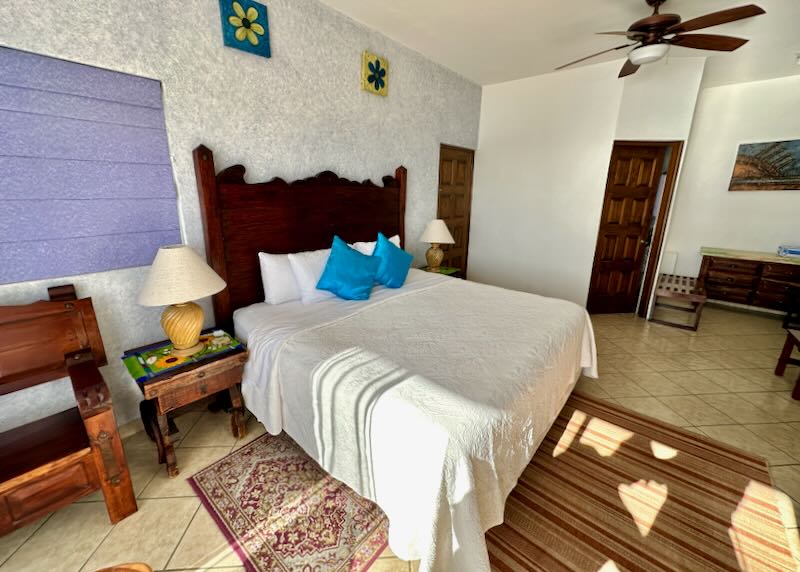 A bed covered in white has a dark wood headboard and orange rugs under it.