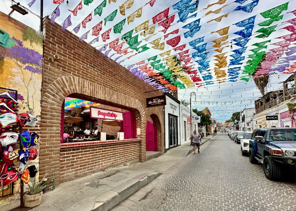 Colorful flags blow in the wind above a stone street in a historic downtown.