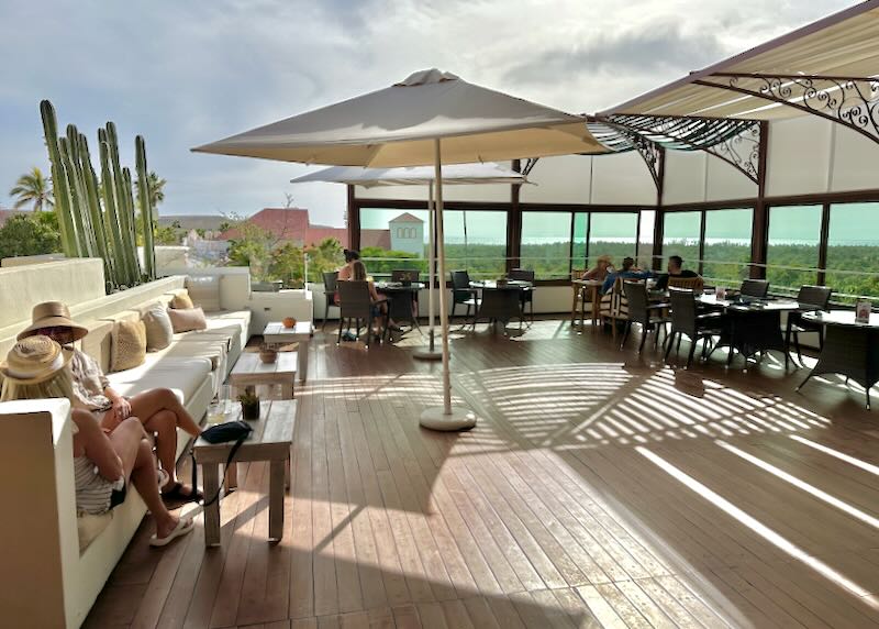 People sit at a rooftop restaurant with views of tree tops and the Pacific ocean.