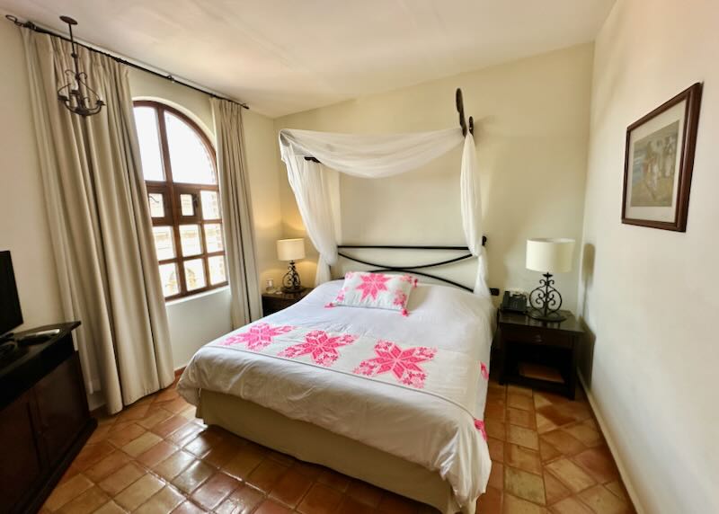 A hotel room with a pink embroidered pillow and throw blanket.