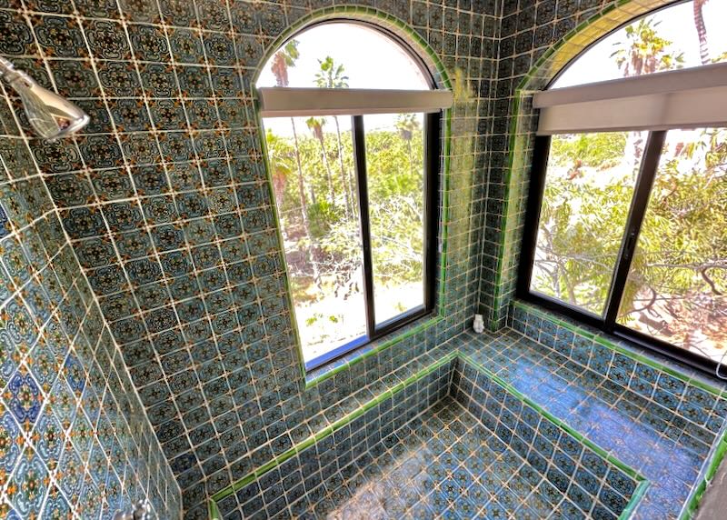 A blue and green tiled shower with windows to the outside.