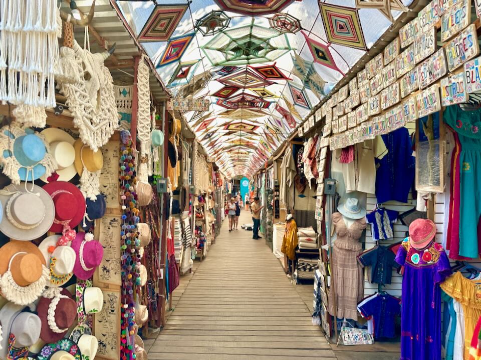 A covered market with a wooden walkway and God's eyes overhead.