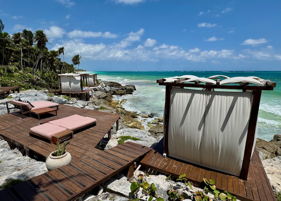 A collection of wooden sun decks with cabanas and pink sunbeds perched on a rocky shore above the ocean at Mi Amor Hotel in Tulum.