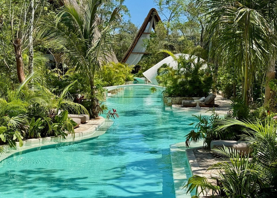 A long, winding pool in a lush jungle setting with an A-frame building in the back at Milam hotel in Tulum.