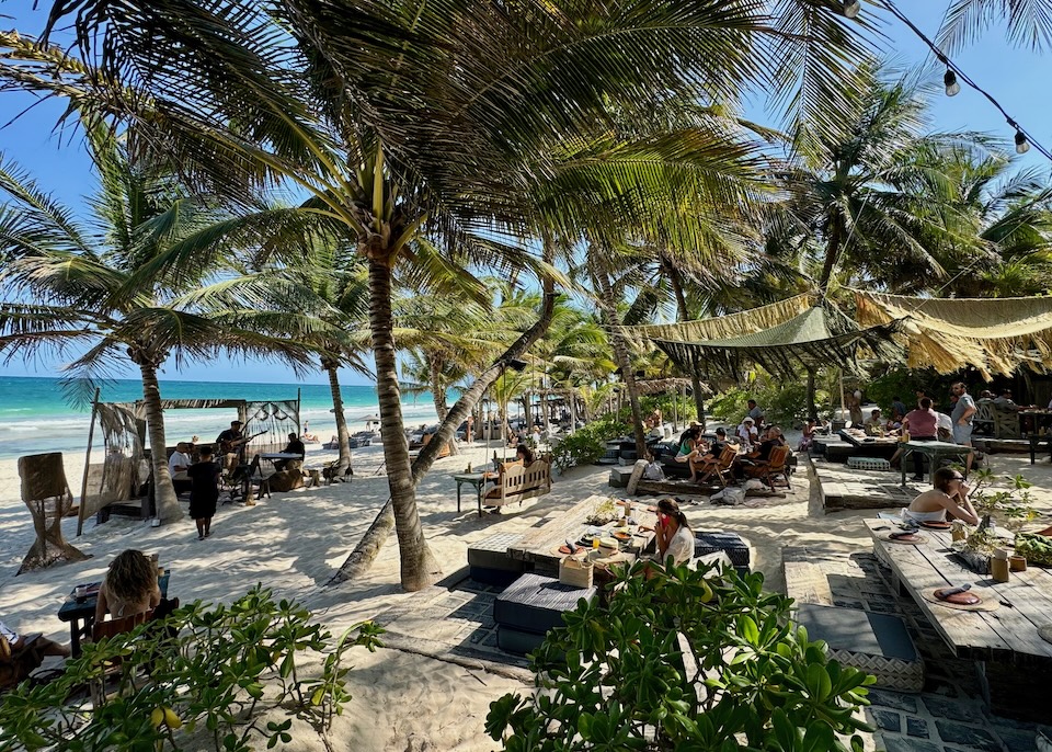 Several people enjoying live music at a beach club with palm trees and macrame canopies at Nomade hotel in Tulum.