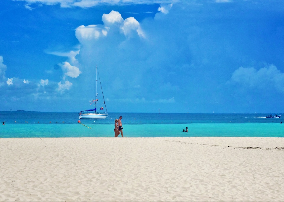 A couple walking on the beach with a sailboat in the background in the North Hotel Zone of Cancun.