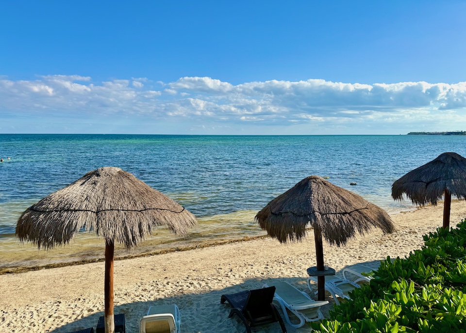 Thatched umbrellas shading some sunbeds on a beach in the Riviera Cancun.