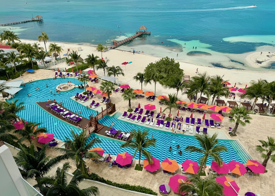 A whimsical pool with a swirl at one end and checkerboard pattern with bright umbrellas above the beach at Breathless Resort in Cancun.