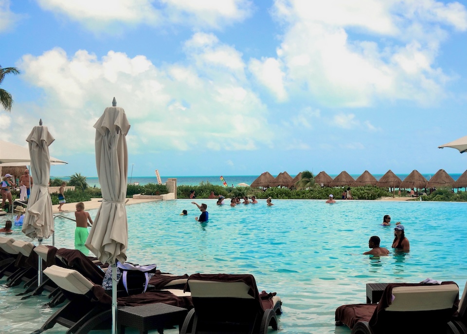 People enjoying a pool with an ocean view at Dreams resort in Playa Mujeres near Cancun.