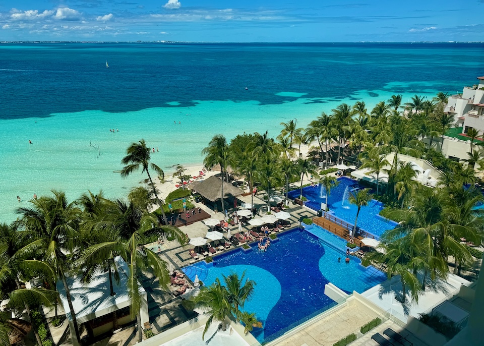 Side-by-side pools with palm trees behind the beach at Dreams Sands in Cancun.