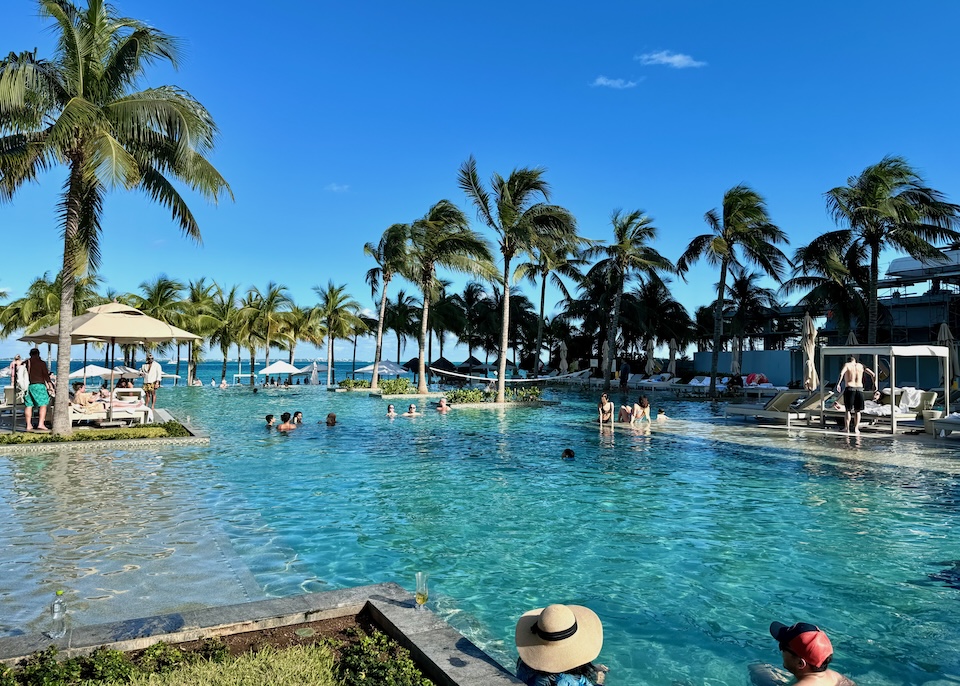 People enjoying a large infinity pool under palm trees facing the ocean at Garza Blanca resort in Playa Mujeres near Cancun.