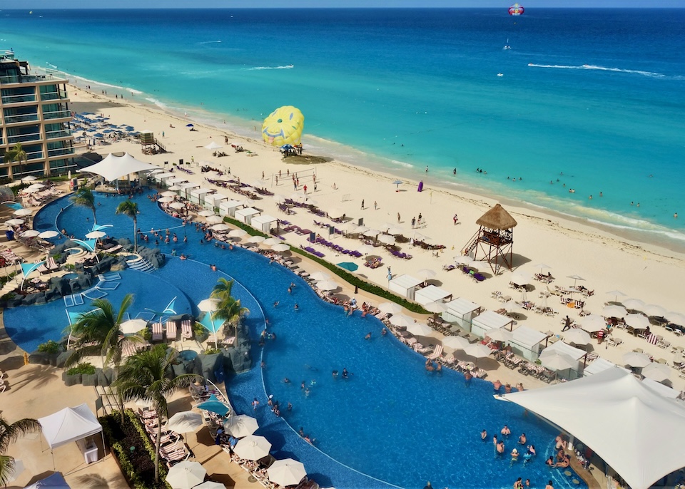 An enormous pool running longways behind the beach with sunbeds and umbrellas at the Hard Rock resort in Cancun.