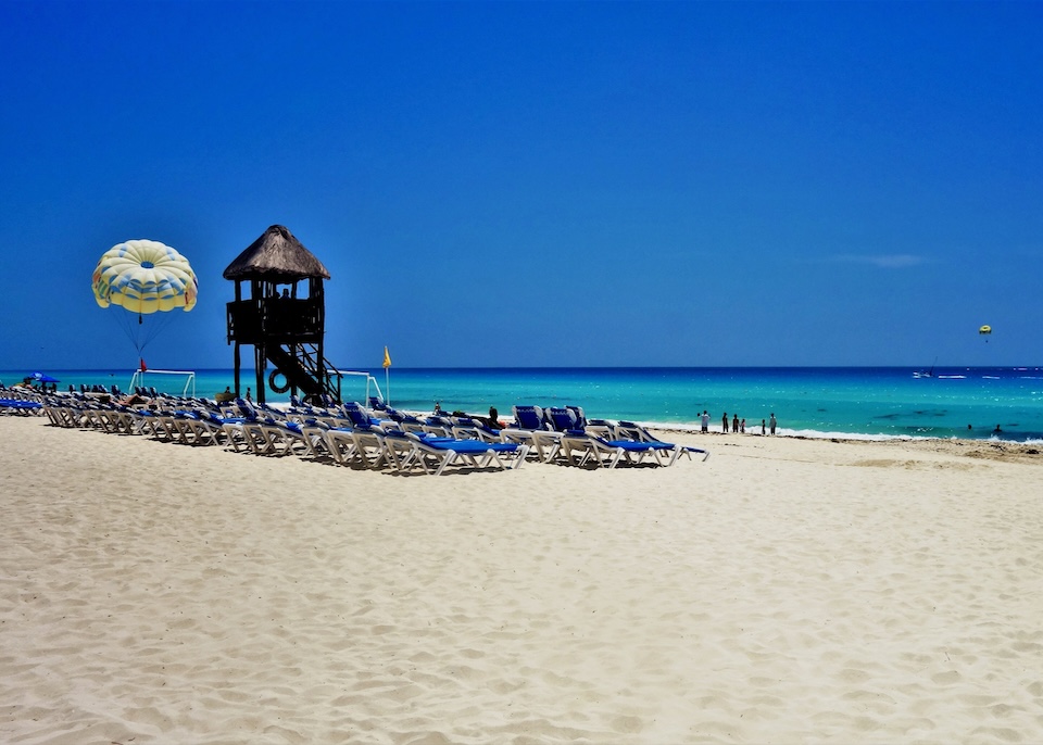 A group of sunbeds next to a lifeguard stand with parasailing canopies in the air at the Marriott resort in Cancun.