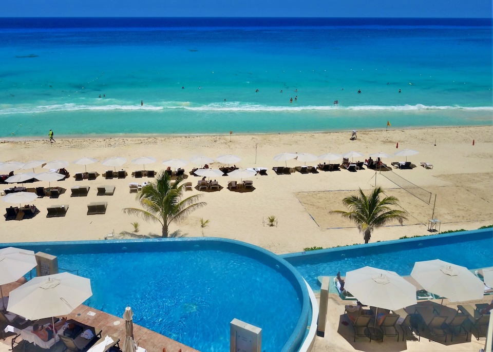 Two pools overlooking the beach with sunbeds and umbrellas at Sun Palace resort in Cancun.