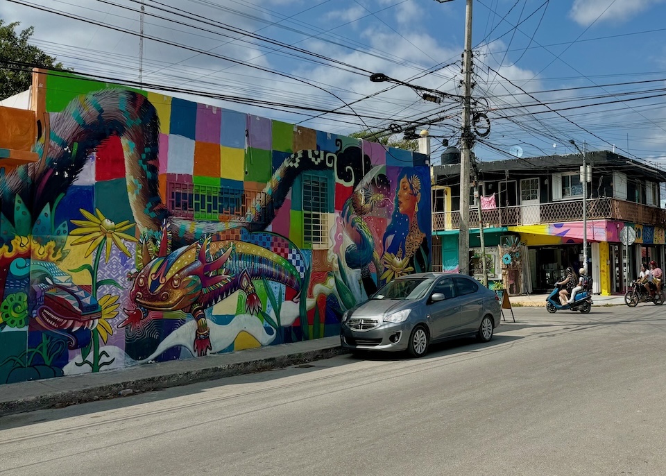 An elaborate, colorful mural featuring the winged serpent god, Kukulkan, an axolotl, and a jaguar woman on a street in Tulum Pueblo.