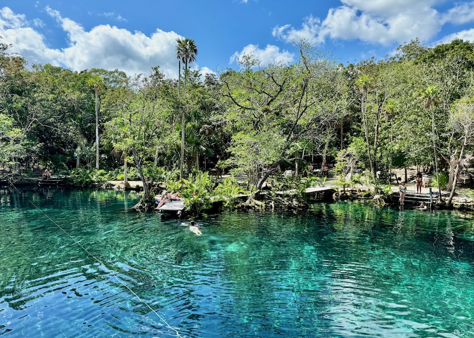 People swimming and relaxing on a dock at Cenote Corazón del Paraíso in the jungle in Tulum.