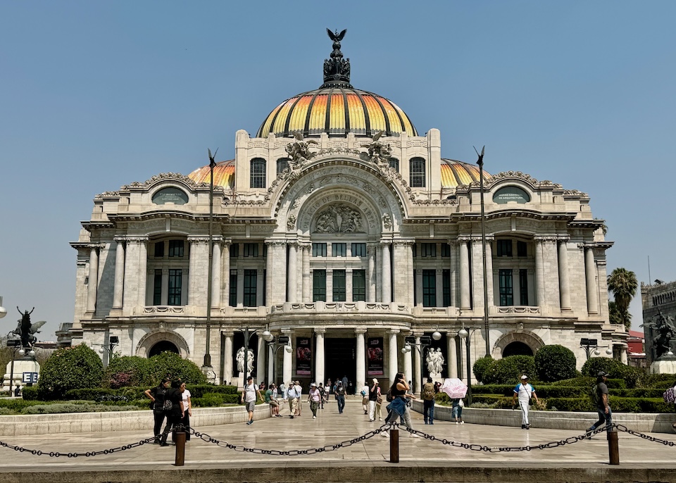 The opulent Palacio de Bellas Artes features an Art Nouveau and Neoclassical exterior with a domed roof, columns, arches, and manicured gardens in Centro Historico.