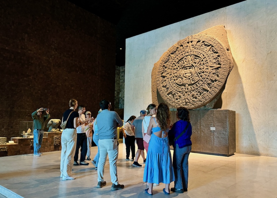 The Aztec Sun Stone on display with visitors milling around in the National Museum of Anthropology.