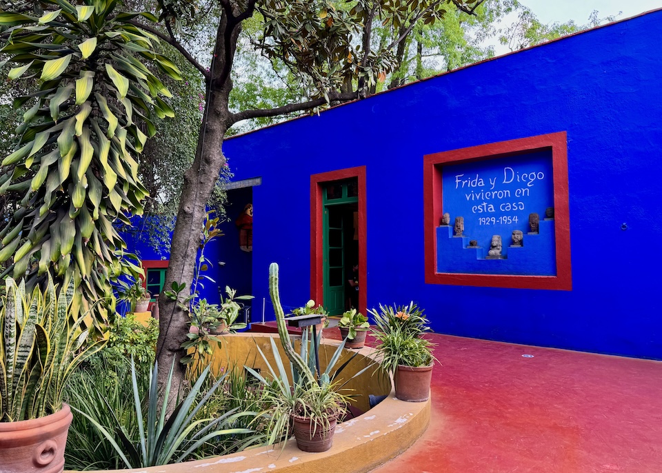 A vivid blue wall with the words "Frida y Diego vivieron en esta casa 1929-1954" written on it and a cactus garden in front at the Frida Kahlo Museum in Coyoacán, Mexico City.