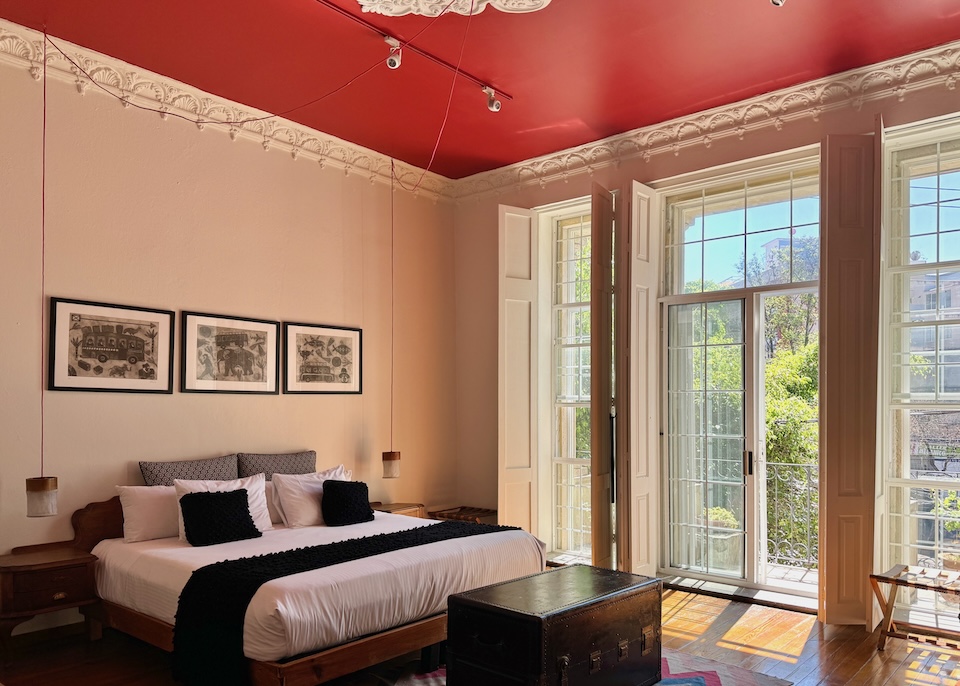 A sunny room with a wall of windows, a red ceiling, and contemporary furnishings in an elegant 1890s mansion at El Patio 77 in San Rafael, Mexico City.