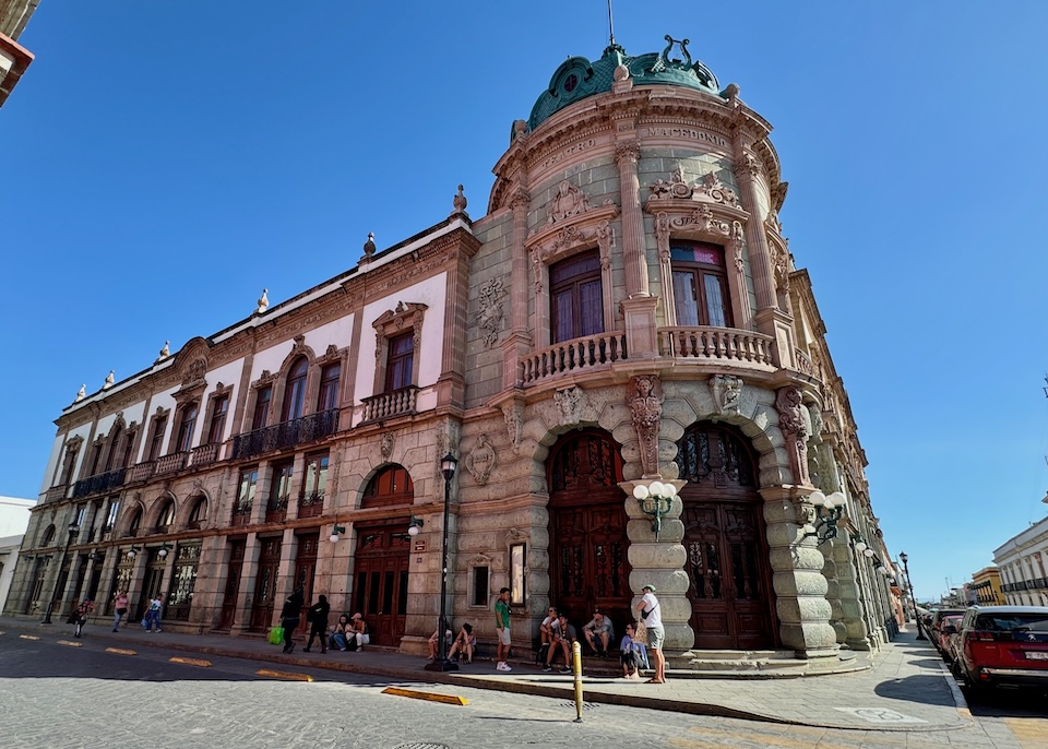 The ostentatious Art Nouveau facade of Teatro Macedonio Alcala with arches, Corinthian columns, busts, and a dome in the Centro neighborhood of Oaxaca.