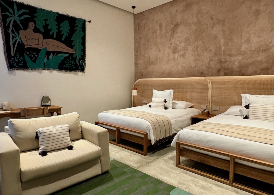 A chic two-bed suite with a wall textile nude, neutral palette, and green accents at Casa Antonieta hotel in Oaxaca.