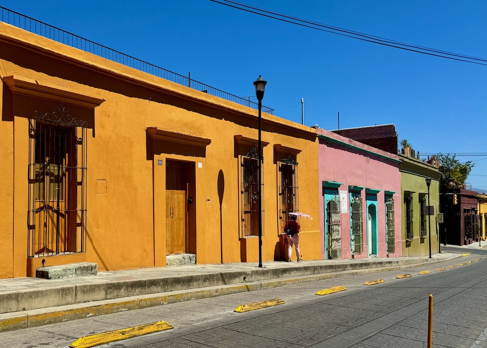 Deep golden exterior of the single-story Casa Carmen Morelos hotel on a gentle hill in a row of colorful buildings in Oaxaca.