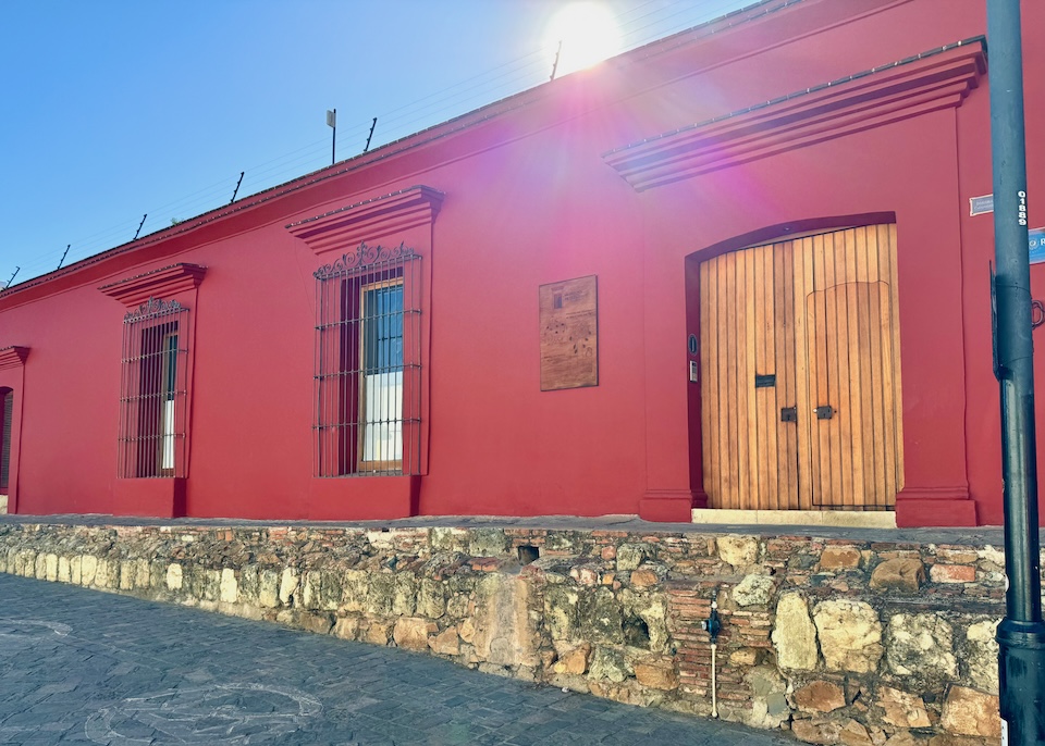 Deep red exterior of the hotel Casona de Tita, built on an elevated stone walkway with wooded double doors in Oaxaca.