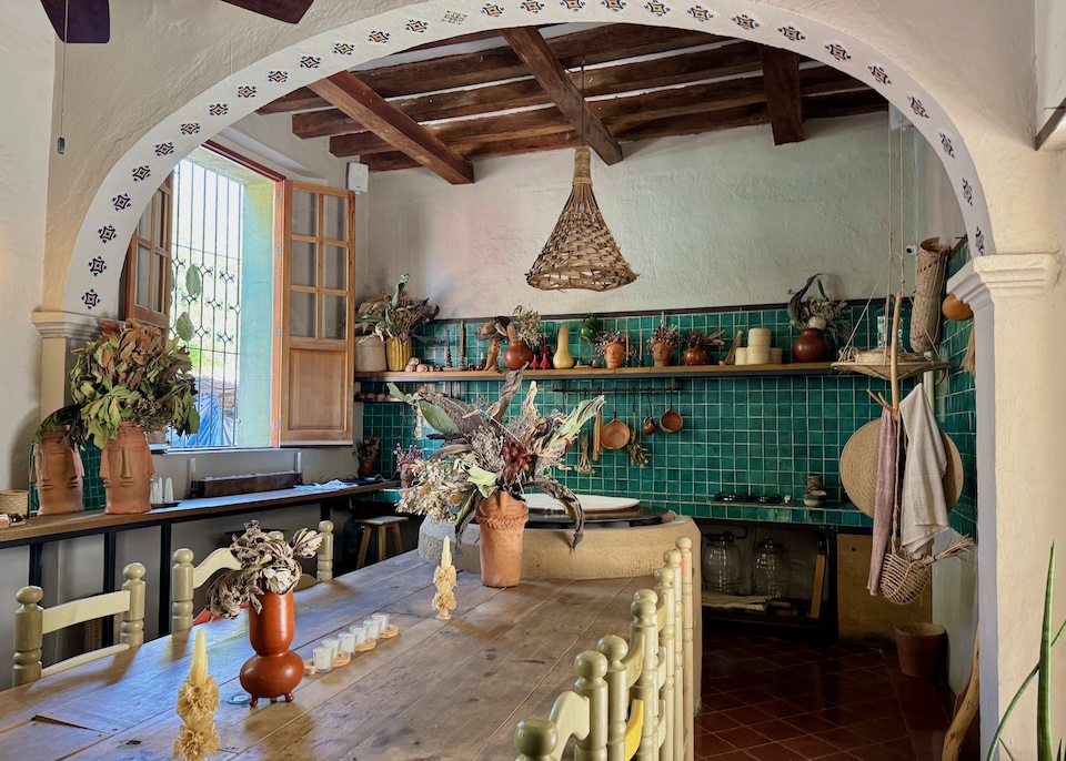 A homey kitchen with a green tile backsplash, stenciled archway, comal, and long wooden breakfast table at Grana B & B in Oaxaca.