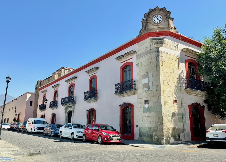 The pale pink with red trim exterior of Quinta Real hotel, set in a 16th-century colonial building with a clock tower as a corner in Oaxaca.