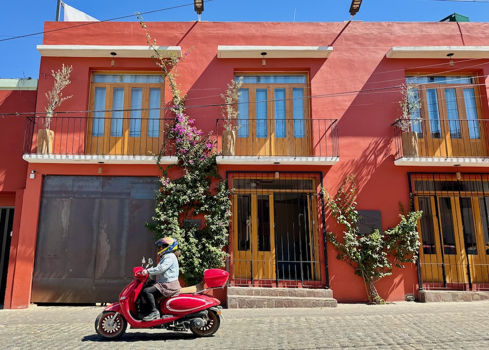 Bright red, two-story Hotel Santa Cecilia, set on a slight hill with a scooter zooming by in Oaxaca.