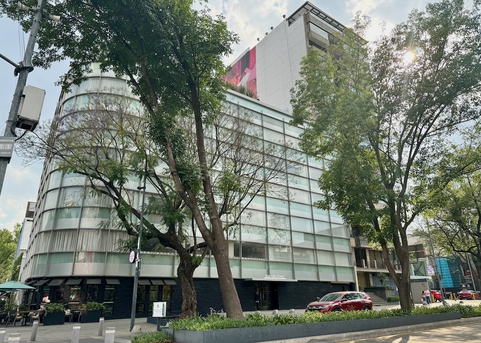 Stylish, 1950s glass and steel exterior of Las Alcobas luxury hotel on a tree-lined street in Mexico City.