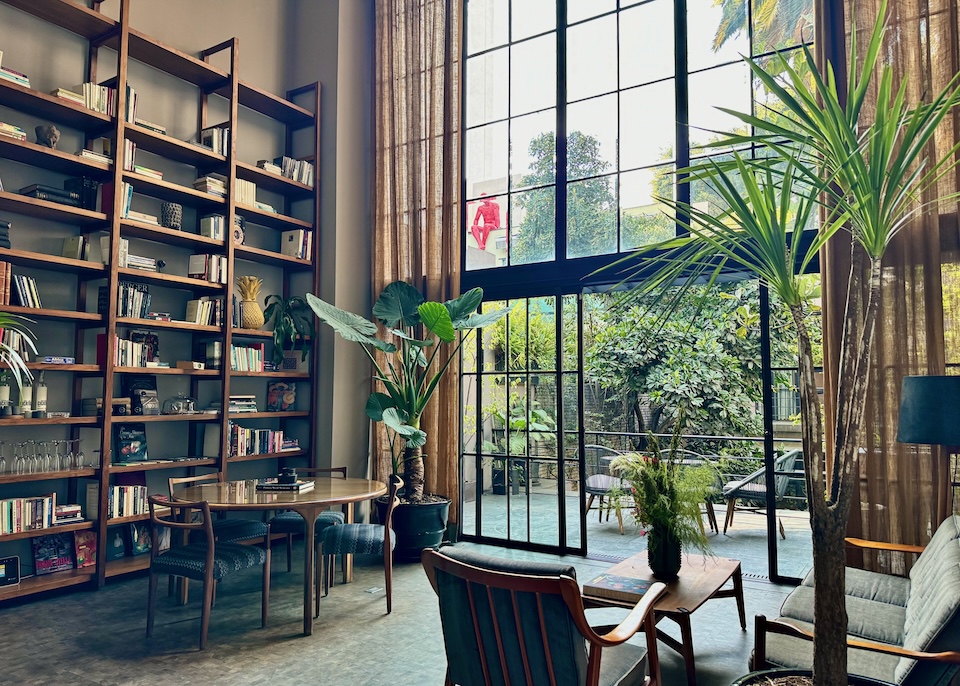 Inside the lobby library with a two-story wall of windows opening out to a garden courtyard at Casa 9 Condesa hotel in Mexico City.