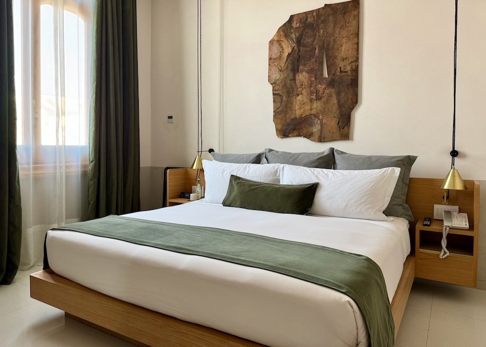 A comfortable, contemporary guest room with brushed brass, moss-green velvet textiles, and rich wood slab wall art at Umbral hotel in Mexico City.